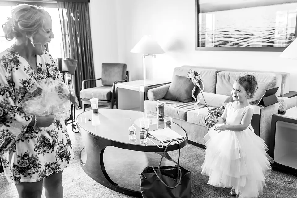 Black and white photo of a flower girl in a tulle dress holding a flower wand in a hotel suite