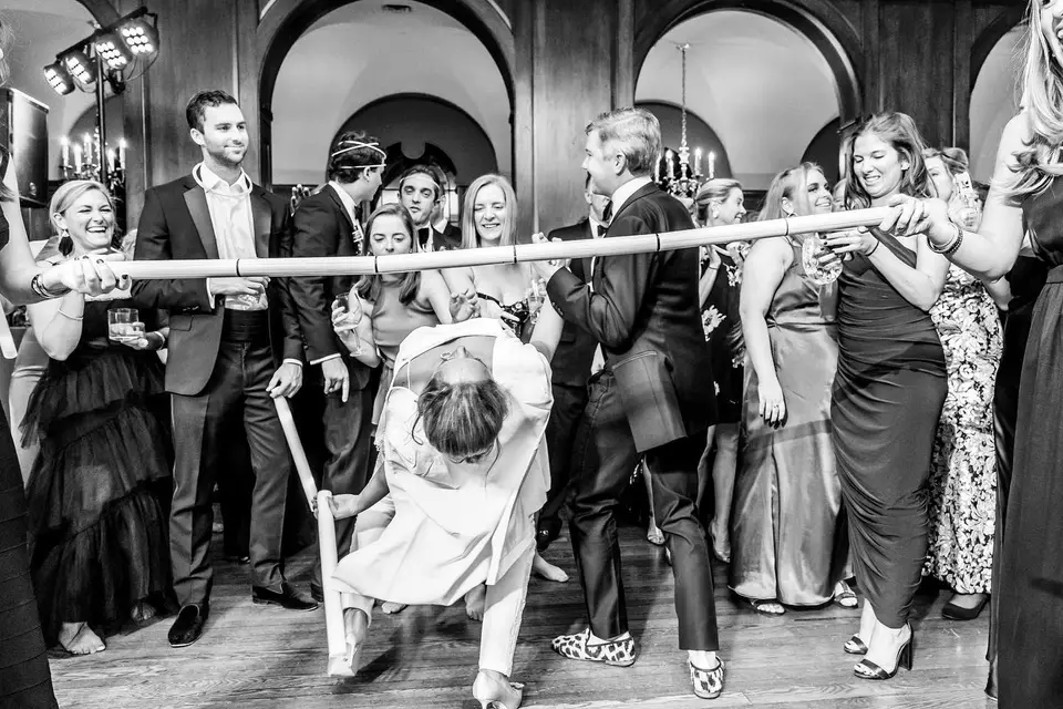 Black and white photo of a guest leaning back under a limbo pole as other guests watch and cheer