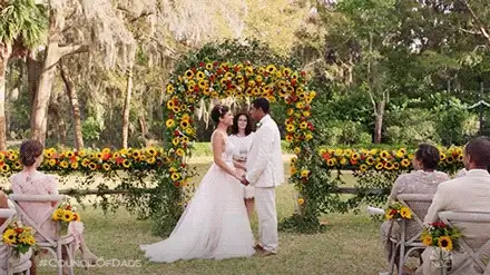Still from a TV wedding scene with a couple exchanging vows under a sunflower arch