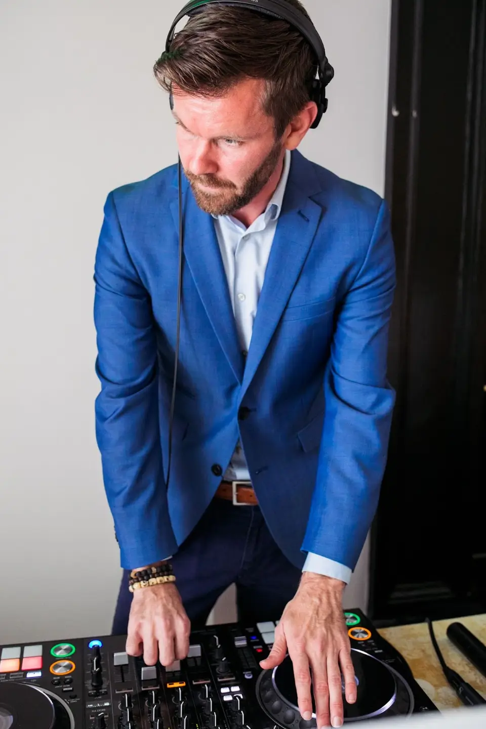 DJ in a blue blazer and headphones leaning over a DJ controller at an event