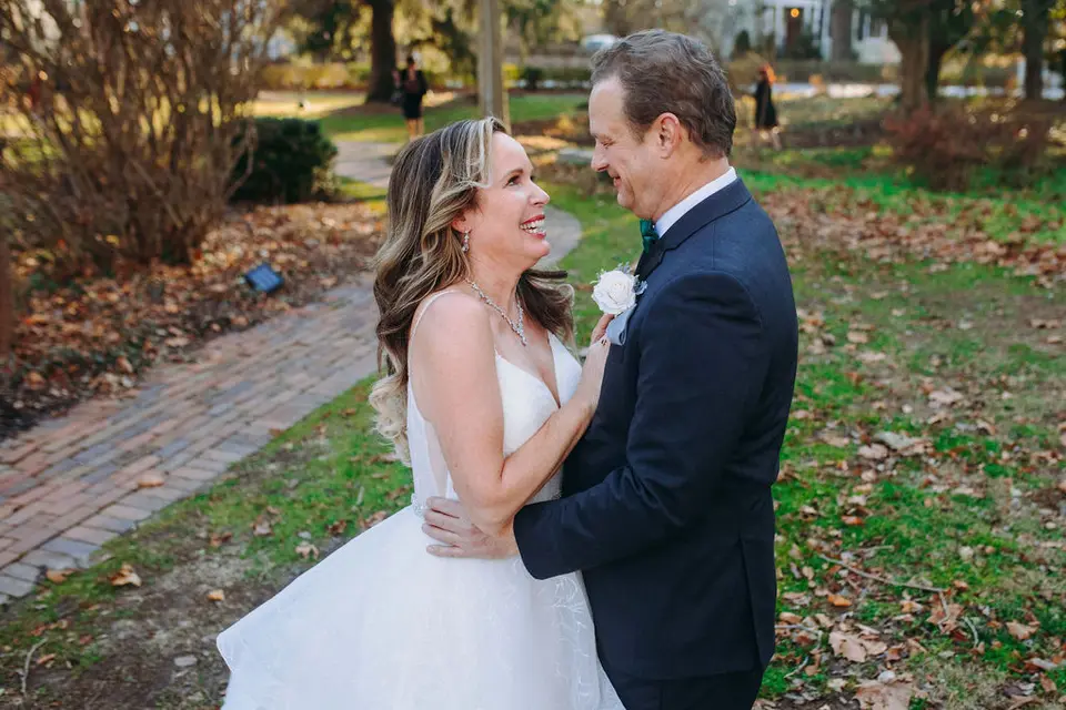 Bride and groom laughing and embracing on a brick path in a park with fallen leaves