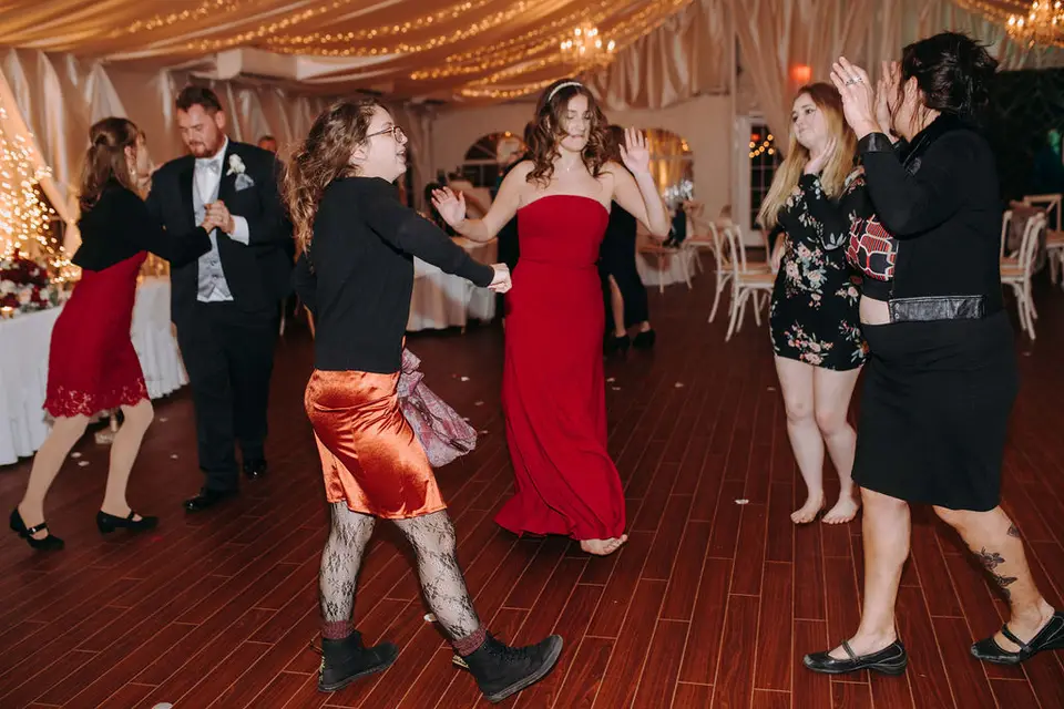 Guests in red and orange dresses dancing and clapping on a wood dance floor in a tented reception