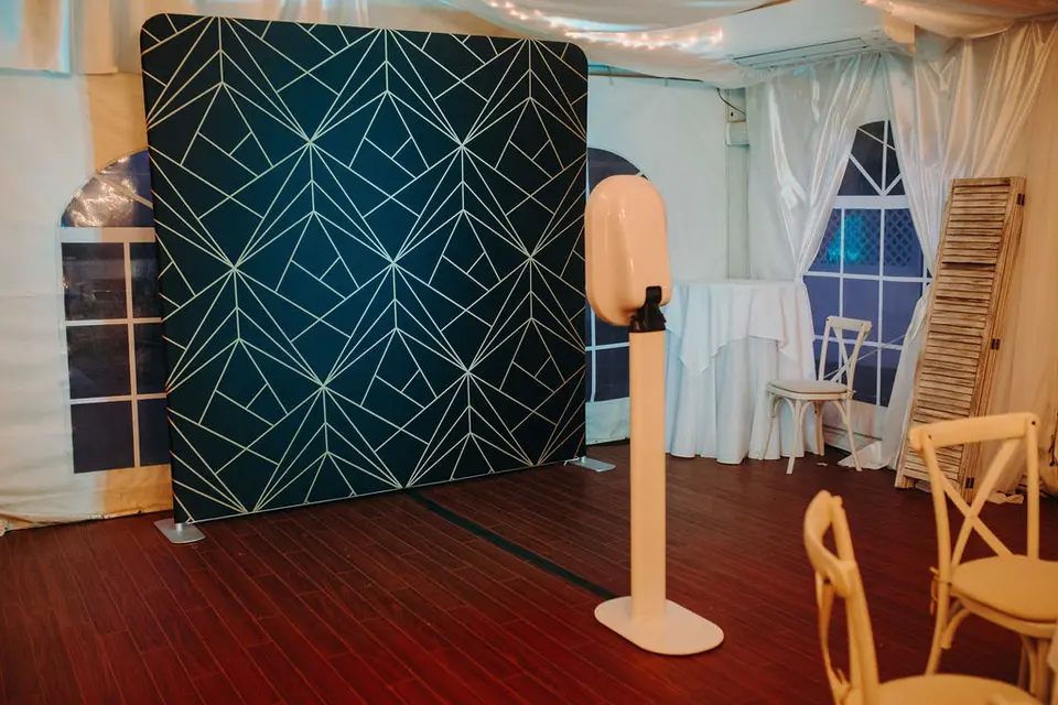 Empty photo booth with a geometric navy and gold backdrop inside a draped reception tent