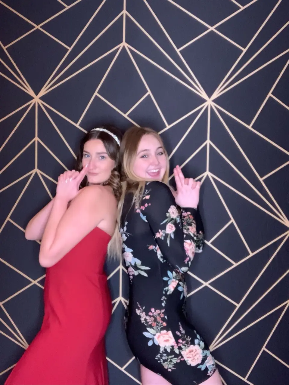 Two women posing back to back in front of a navy and gold geometric photo booth backdrop