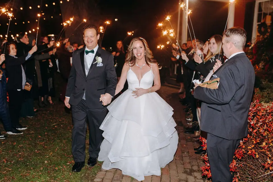 Bride and groom walking hand in hand through a sparkler send-off line of guests at night