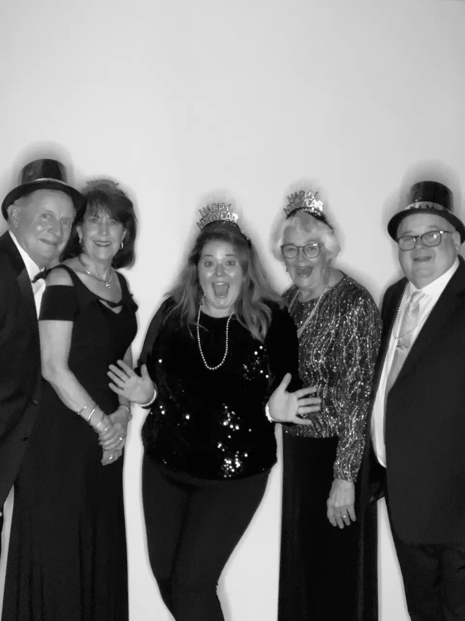 Black and white photo booth picture of five smiling guests in formal wear, three wearing top hats or tiaras