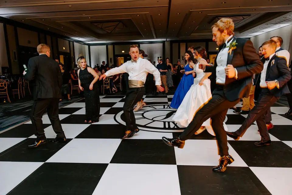 Groom and guests dancing on a black and white checkered dance floor in a hotel ballroom