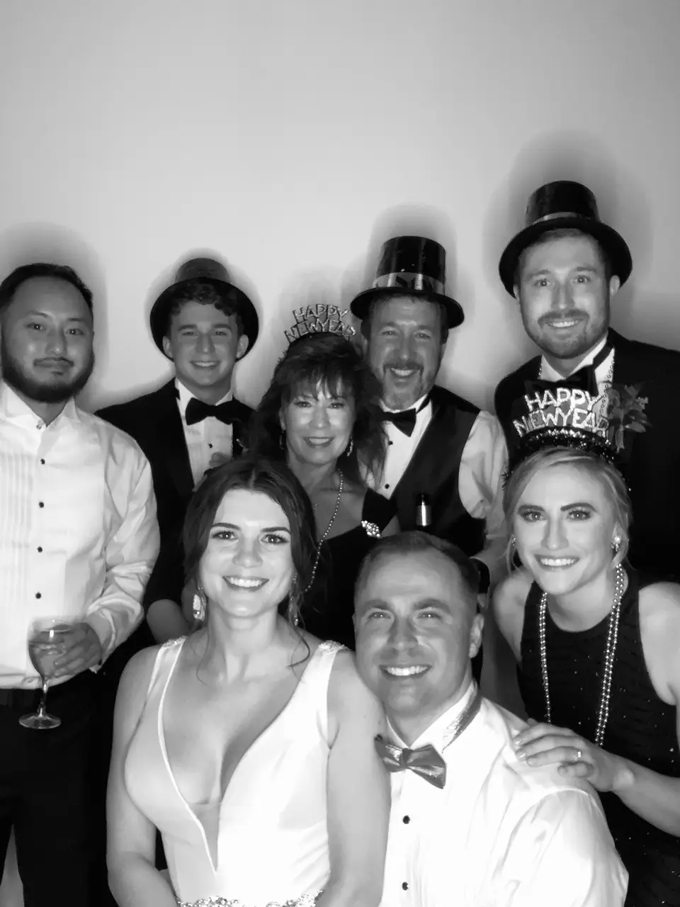 Black and white photo booth group of the couple and guests in formal wear, some wearing top hats and a Happy New Year tiara