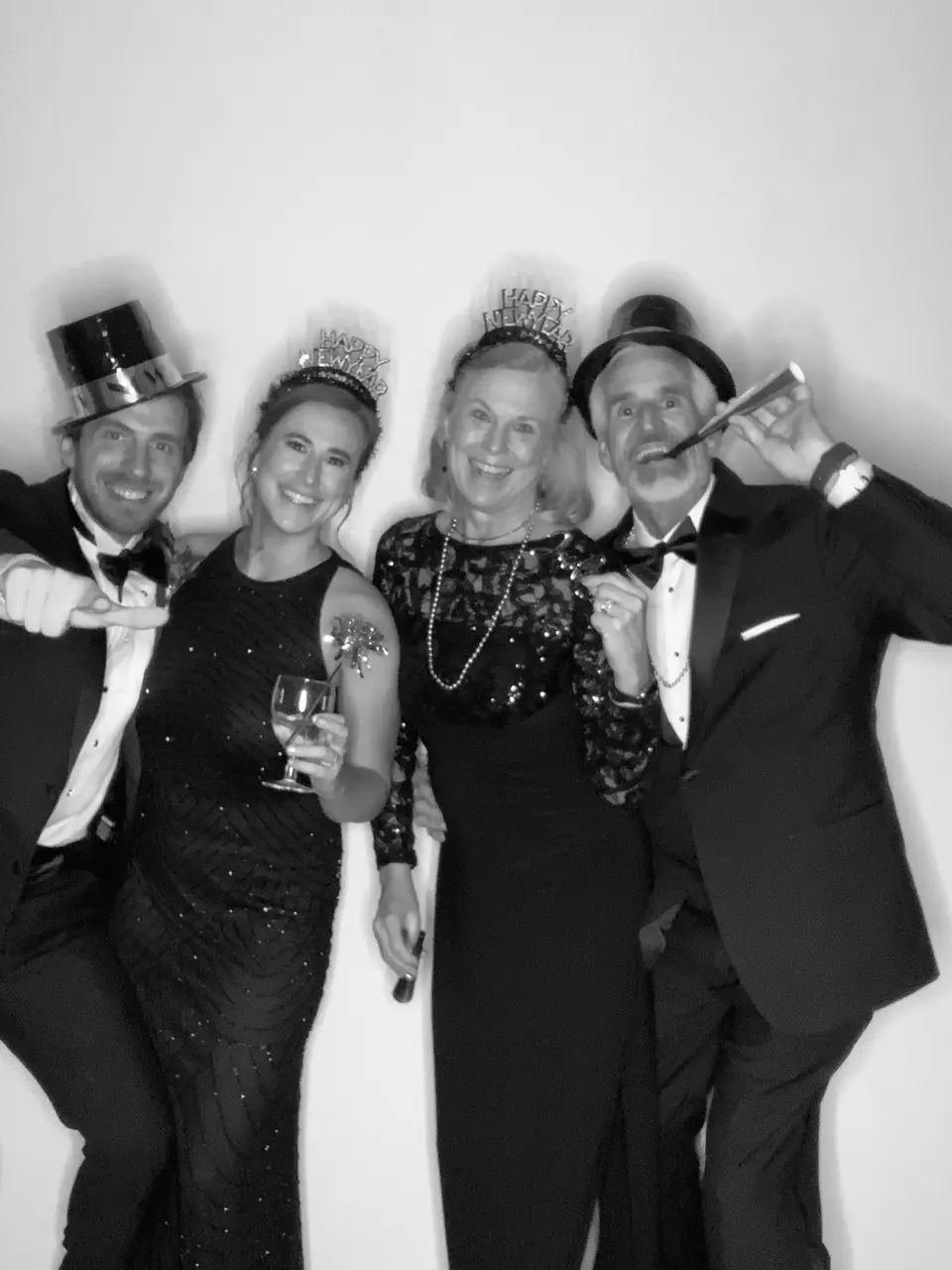 Black and white photo booth picture of four guests in top hats, tiaras and formal wear