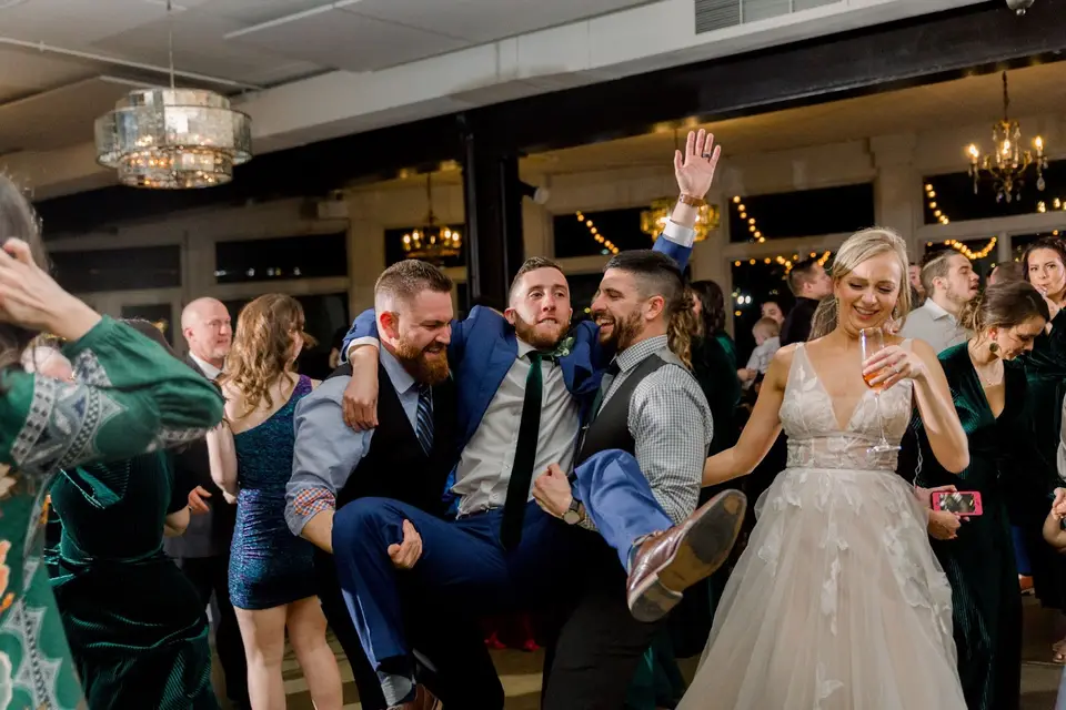 Groom lifted by friends in the air next to the bride while guests dance at the reception