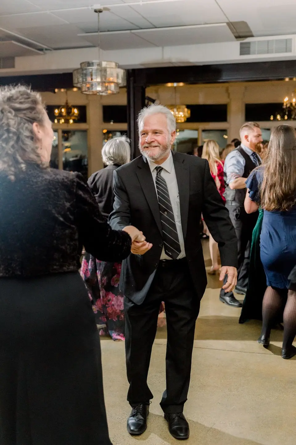 Man in a dark jacket and striped tie smiling and dancing with a guest on the dance floor