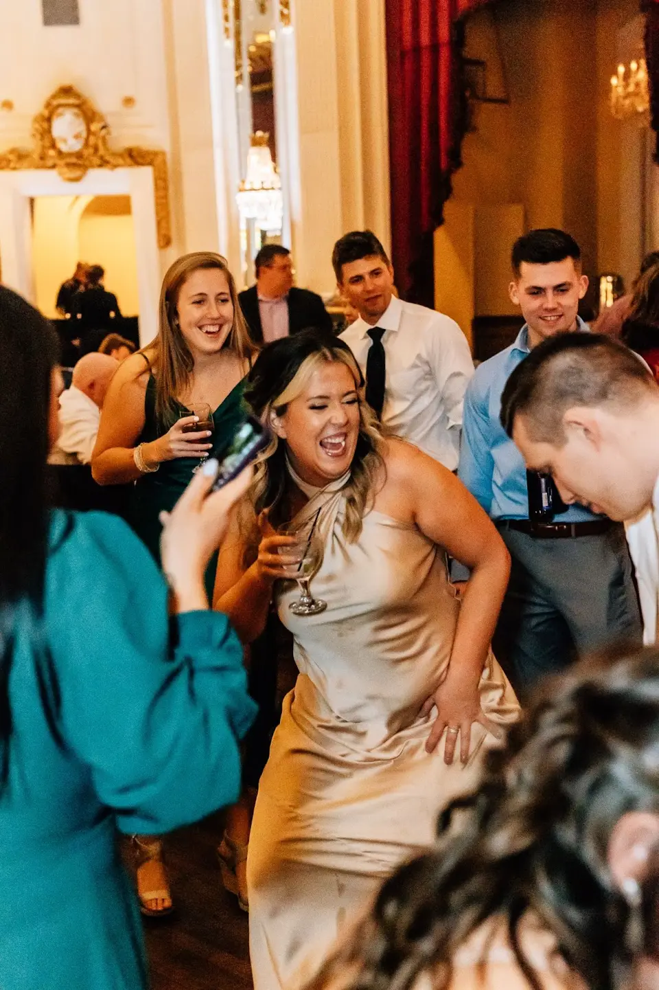 Smiling woman in a champagne satin dress dancing with guests on the dance floor