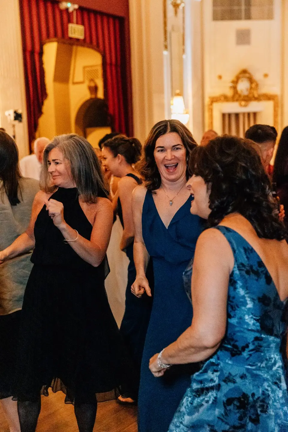 Women laughing and dancing at a wedding reception in an ornate ballroom