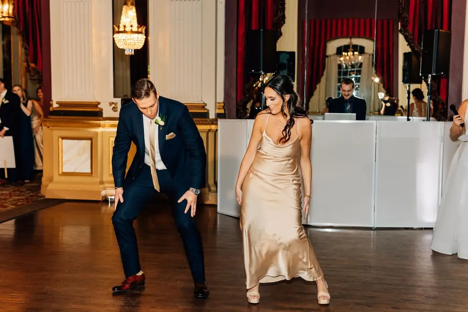Groomsman and bridesmaid dancing on the ballroom floor in front of the white DJ booth