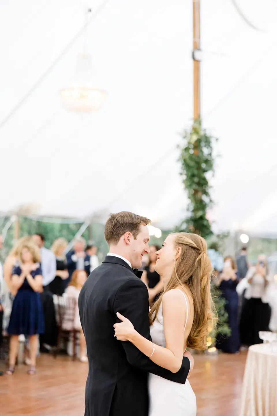 Bride and groom dancing close together under a white tent as guests look on