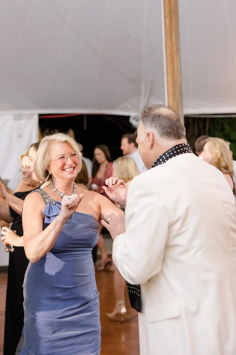 Smiling woman in a blue dress dancing with a man in a white dinner jacket under a tent