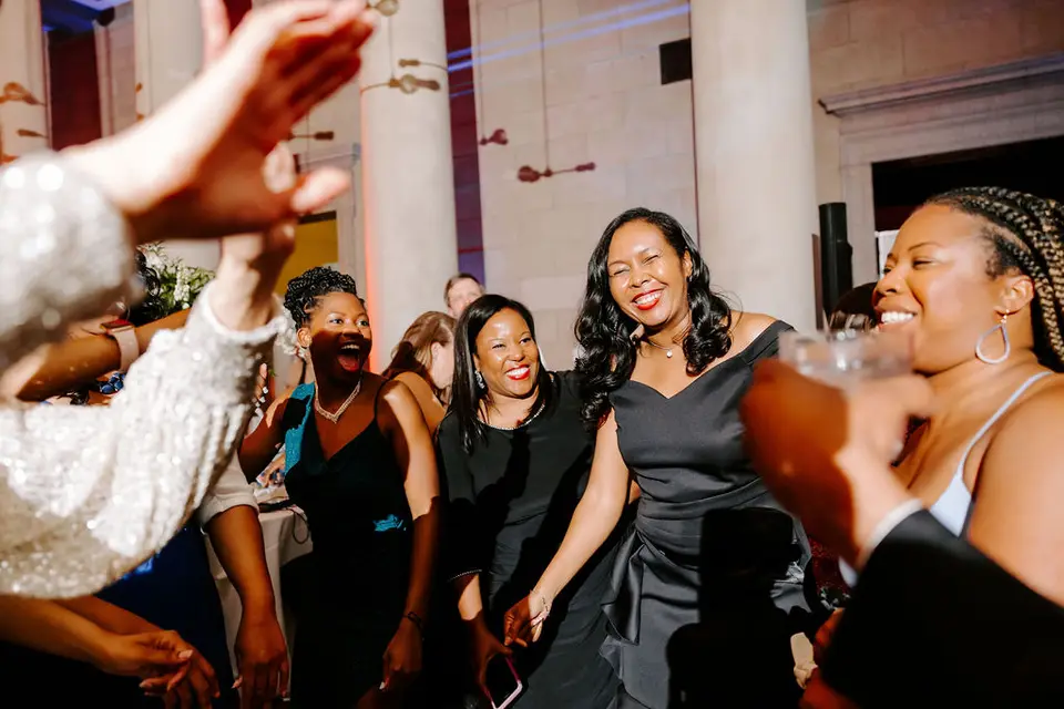 Group of women laughing and dancing at a wedding reception in a columned hall