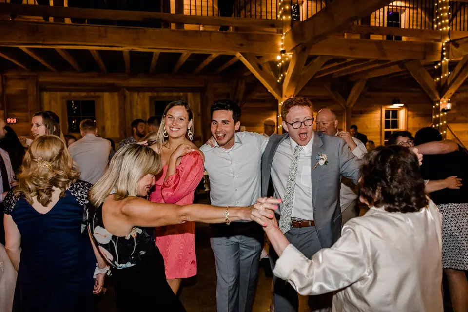 Wedding guests dancing and laughing in a timber-frame barn reception