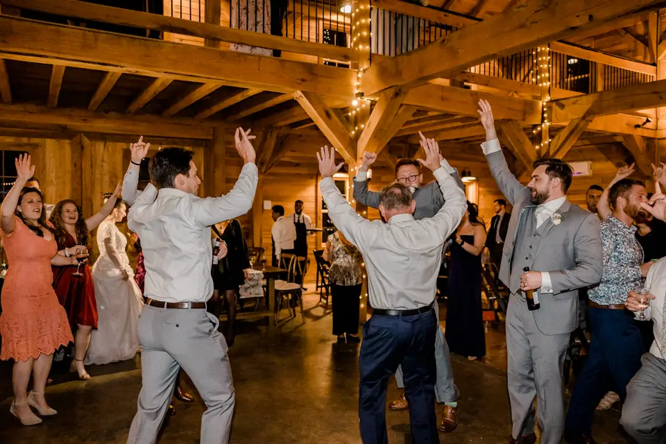 Guests dancing with arms raised in a barn reception under string lights
