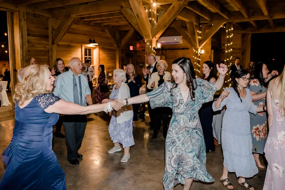 Guests link arms and dance in a circle on a barn dance floor