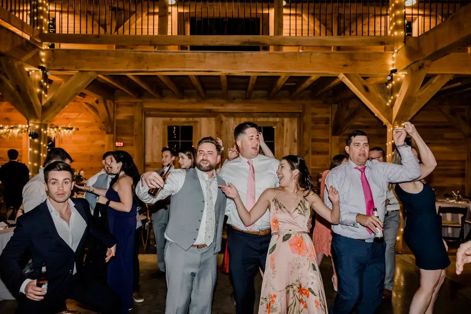 Wedding guests dance and cheer in a barn with string lights overhead