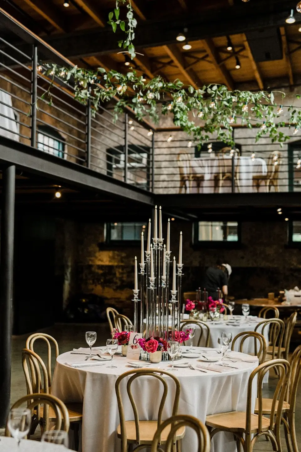 Round reception table with candelabra, pink flowers and gold chairs in a brick venue with a balcony