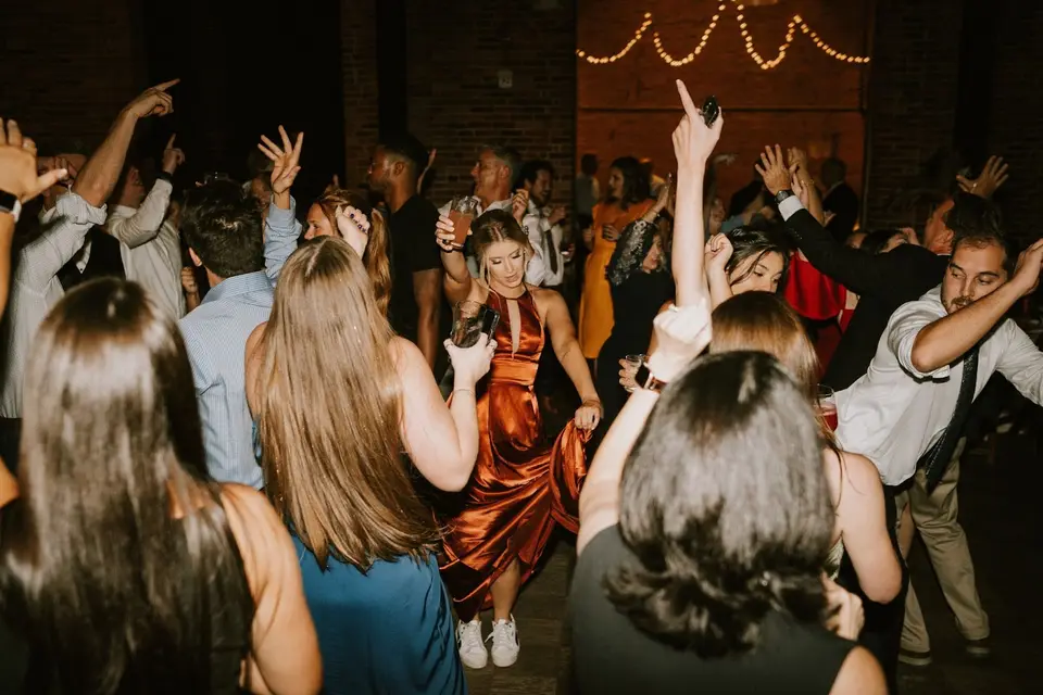 Guests dancing with arms raised on the dance floor, a woman in a copper satin dress in the center