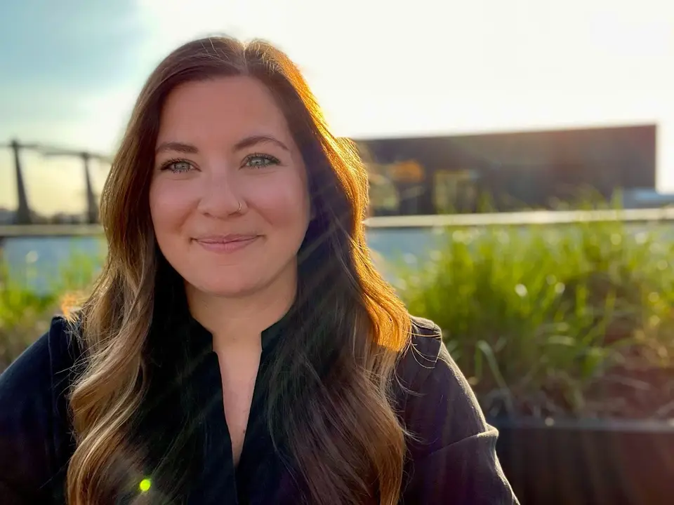 Smiling woman with long brown hair in a dark top outdoors in sunset light