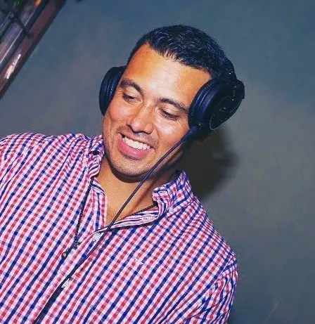 Smiling DJ in a red and blue gingham shirt wearing over-ear headphones