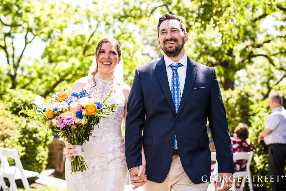 Smiling bride with a colorful bouquet and groom in a navy suit walking up the aisle after their ceremony