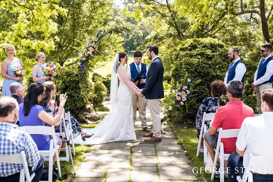Outdoor garden wedding ceremony on a stone path with bridesmaids and groomsmen standing beside the couple