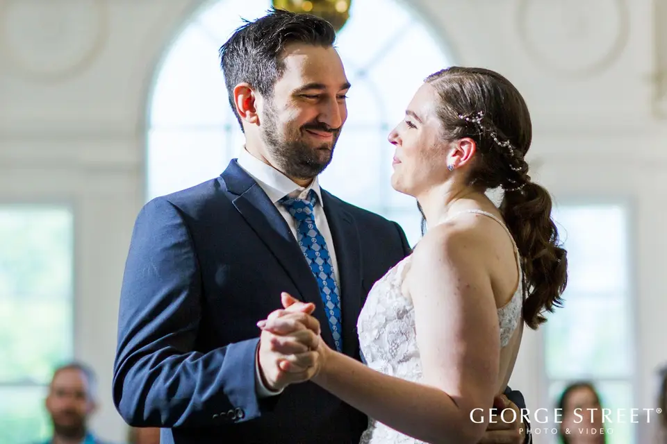 Groom smiling at the bride as they hold hands during their first dance in a bright room