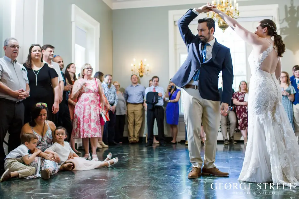 Bride twirling under the groom's arm during their first dance while guests and two children sit on the floor