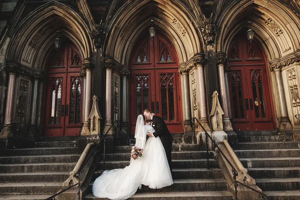 Bride and groom kissing on the stone steps of a church with tall red doors