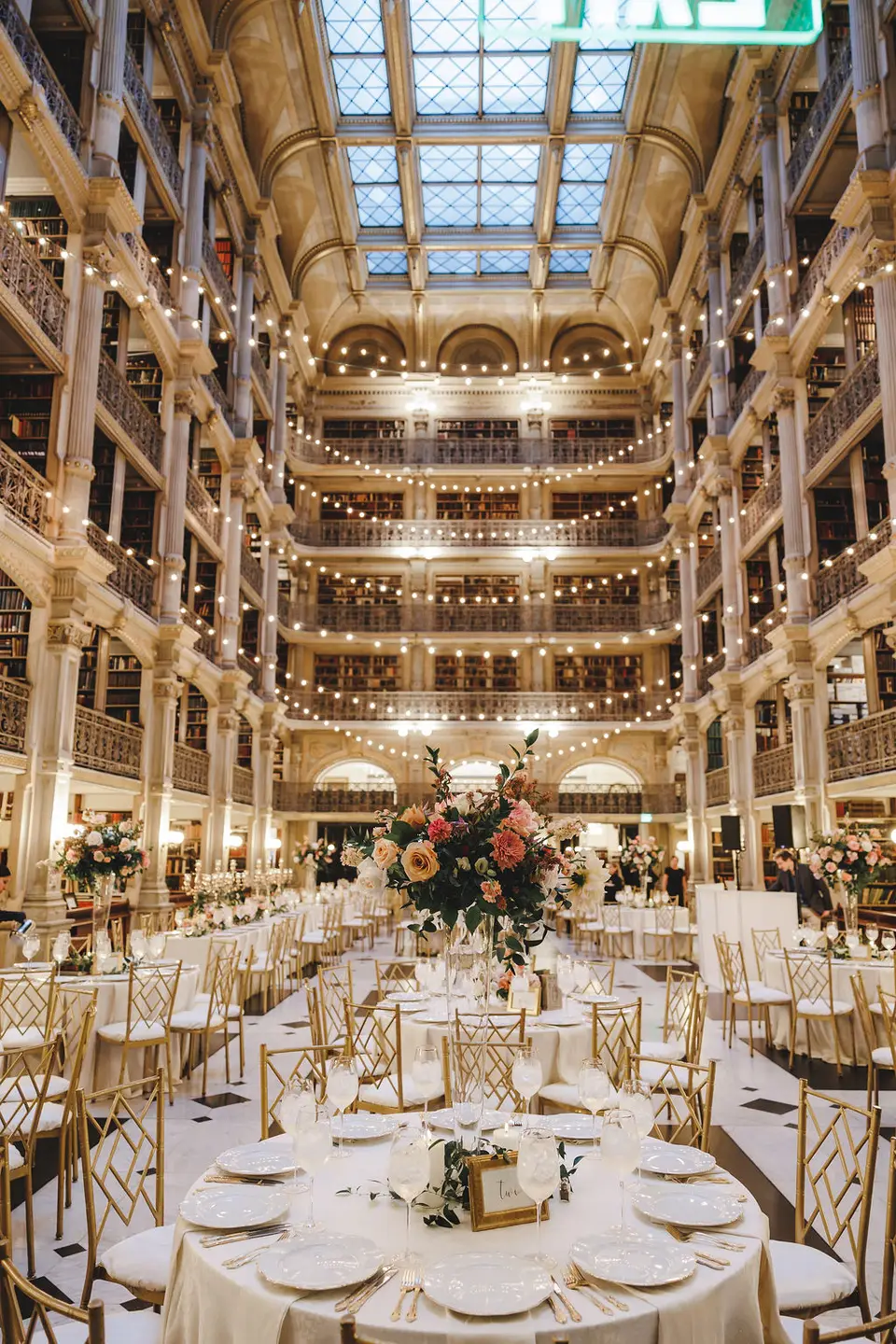 Tiered library hall with string lights and round dinner tables set for a wedding reception