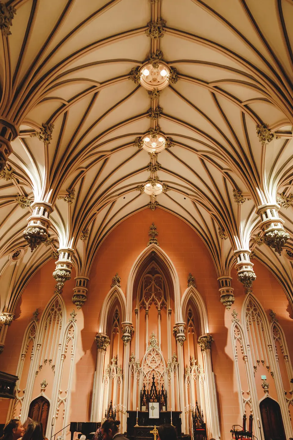 Ornate vaulted church ceiling with chandeliers and pointed arch details above the altar