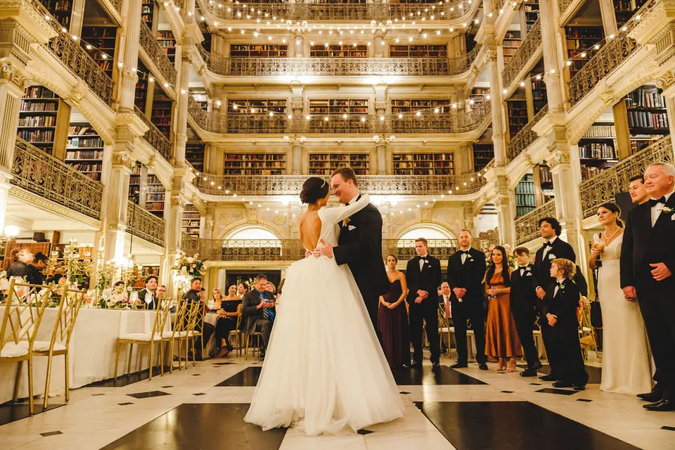 Bride and groom slow dancing in a library hall while the wedding party and guests watch