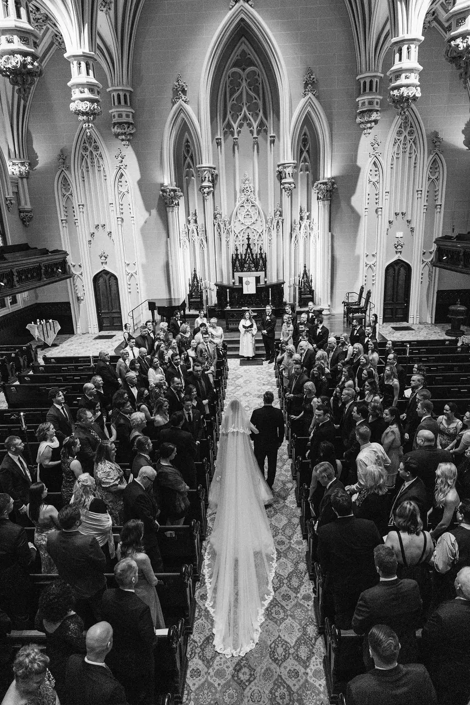 Black and white view from above of a bride walking up the aisle between guests in a Gothic church