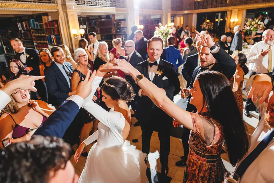 Bride and groom dancing in a circle of cheering guests inside a library venue