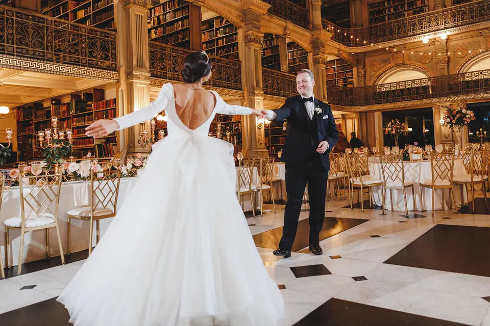 Bride in a gown with a low open back twirling in a ballroom as the groom holds her hand