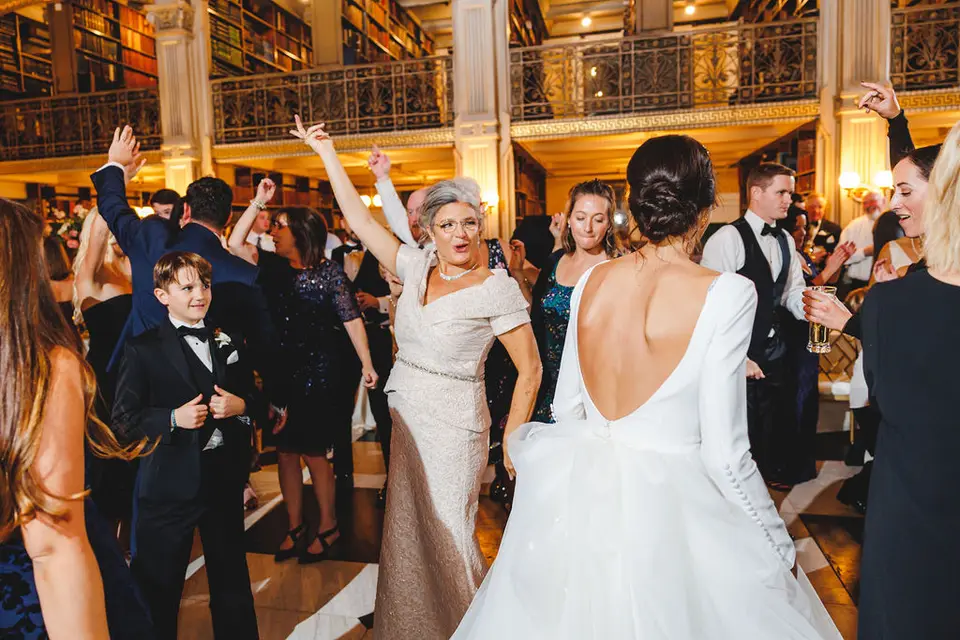 Guests dancing around a bride in a gown, with a boy in a tuxedo and a woman raising her arm