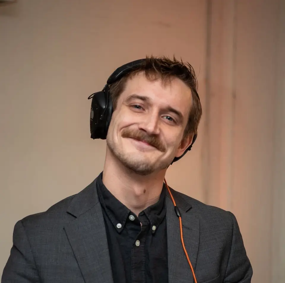 Smiling man with a mustache wearing headphones and a gray blazer