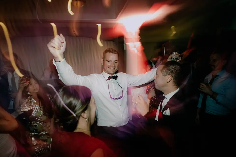 Black and white photo of guests dancing with arms raised at the reception