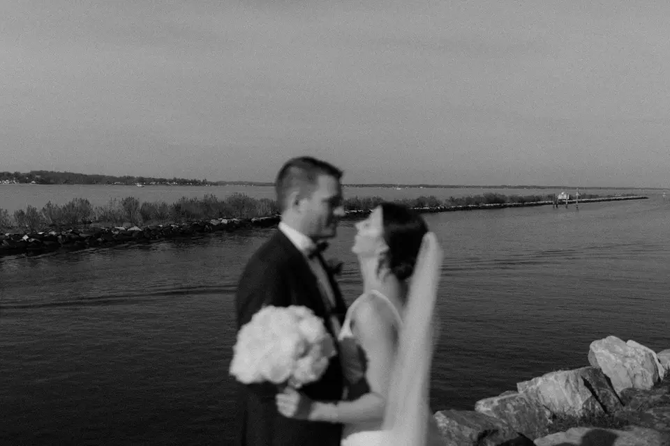 Black and white photo of the bride and groom beside the water, the bride holding a bouquet