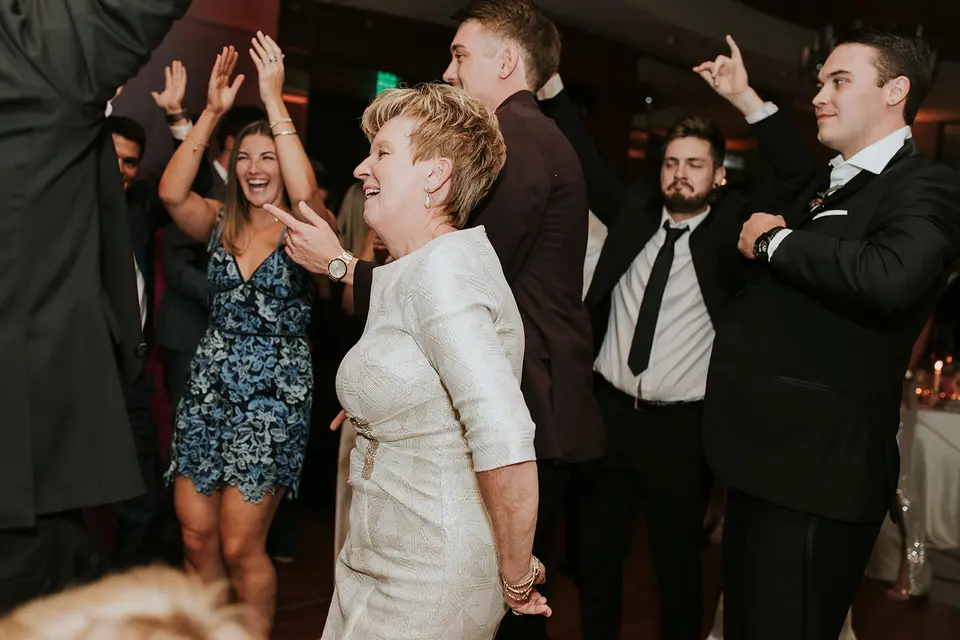Wedding guests dancing and laughing on the dance floor, including an older woman in a silver dress