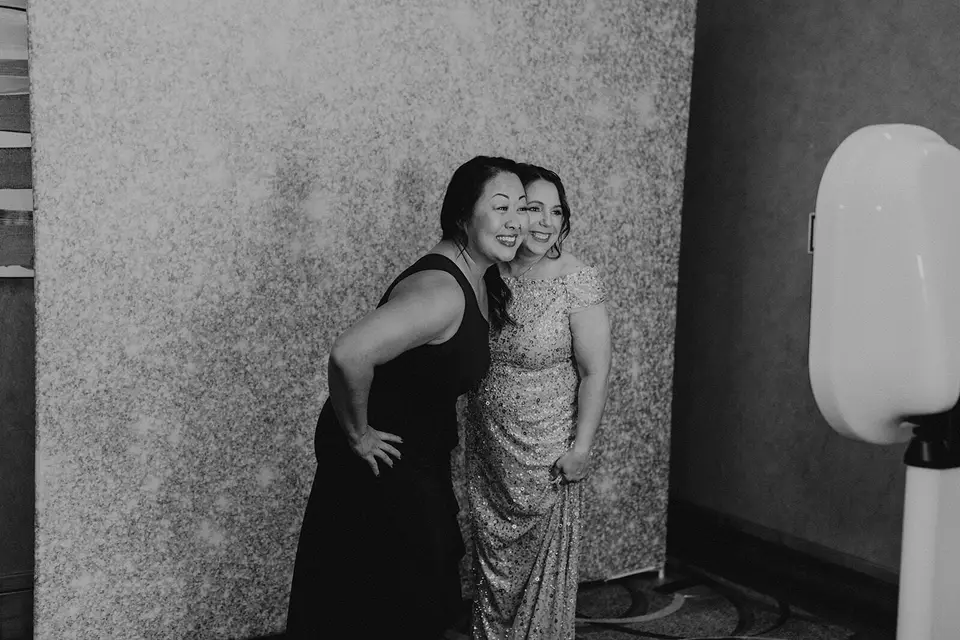 Two women smiling and posing together in front of a glittery backdrop next to a photo booth
