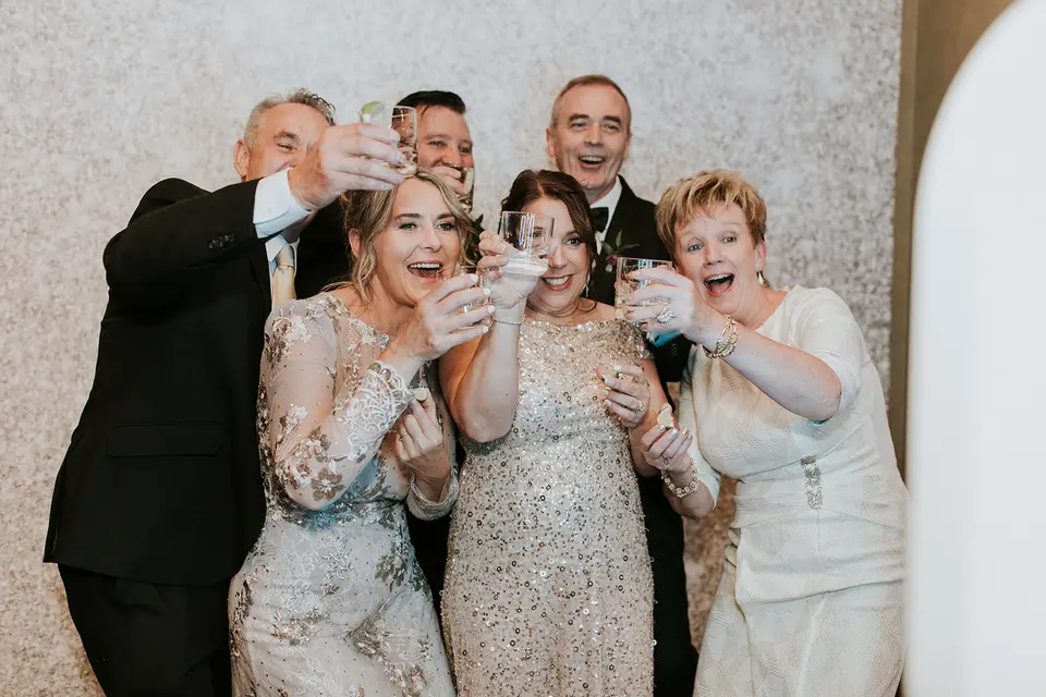 Wedding guests raising glasses and cheering together in front of a sparkly backdrop