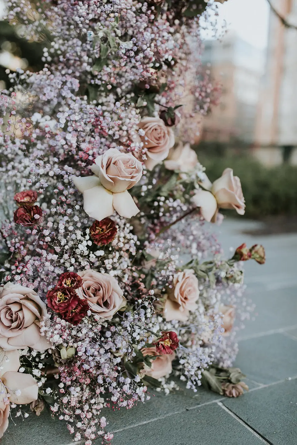 Pink and burgundy roses with baby's breath in a large floral arrangement on the ground at an outdoor ceremony