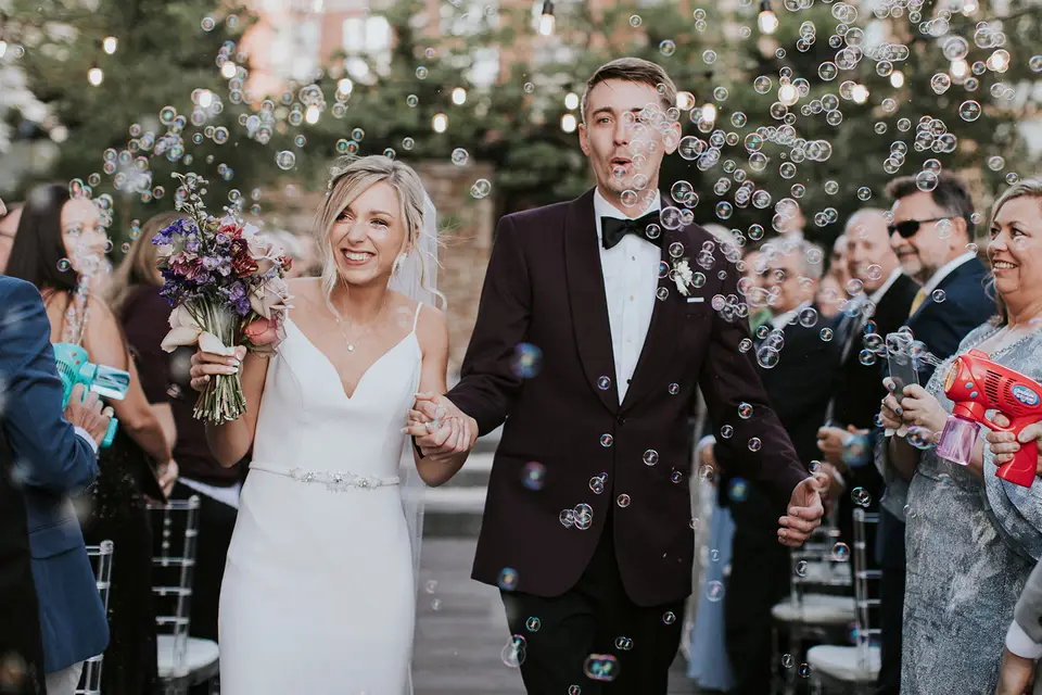Bride and groom walk hand in hand up the aisle through bubbles as guests blow them