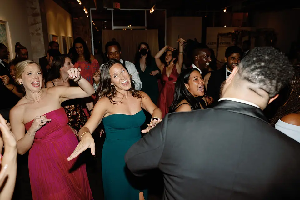 Wedding guests in formal dresses and suits laughing and dancing on a crowded dance floor